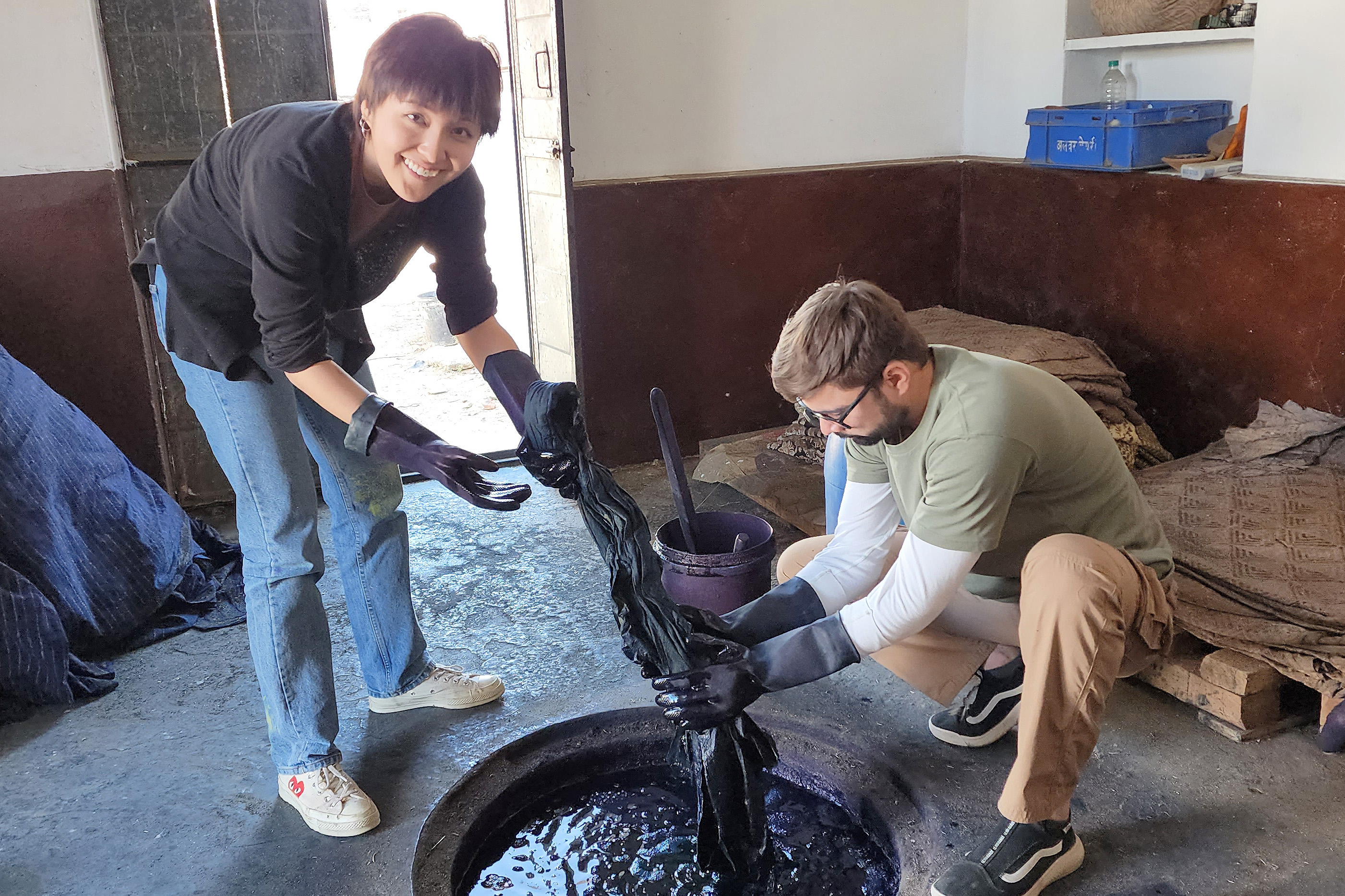 student works with Indian artisan dipping textile into vat of dye