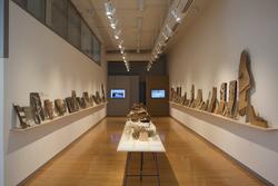 two rows of scale architectural models propped against gallery walls, flanking a long table of several more models