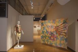 a mannequin wears a colorful skirt and top combo in an art gallery, opposite a colorful hanging print