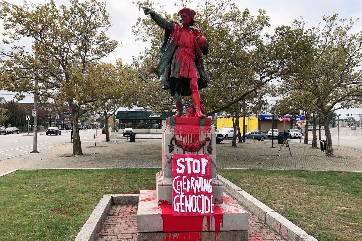 Christopher Columbus statue covered in red paint, with "stop celebrating genocide" sign
