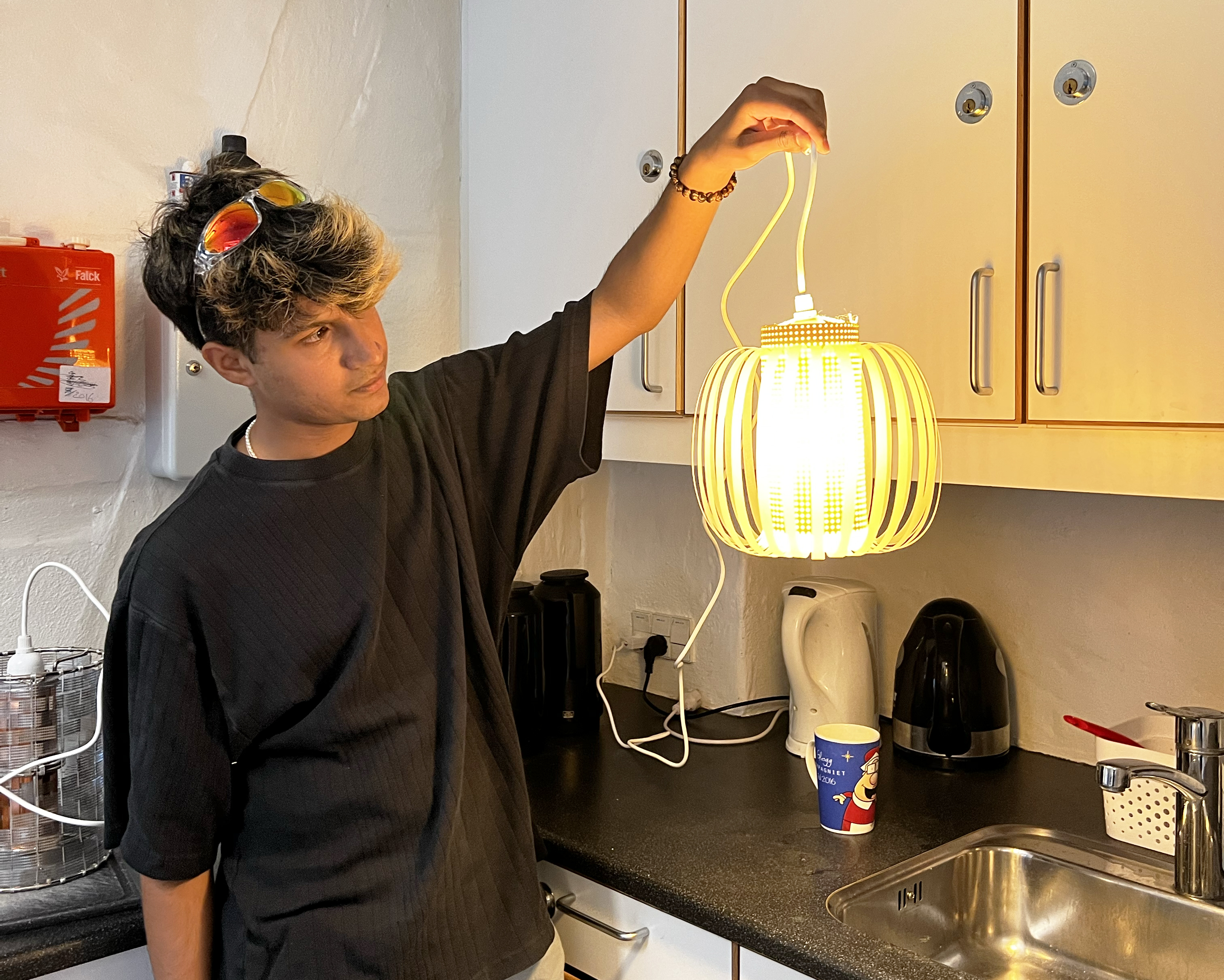 a student holds up a paper lamp he has completed