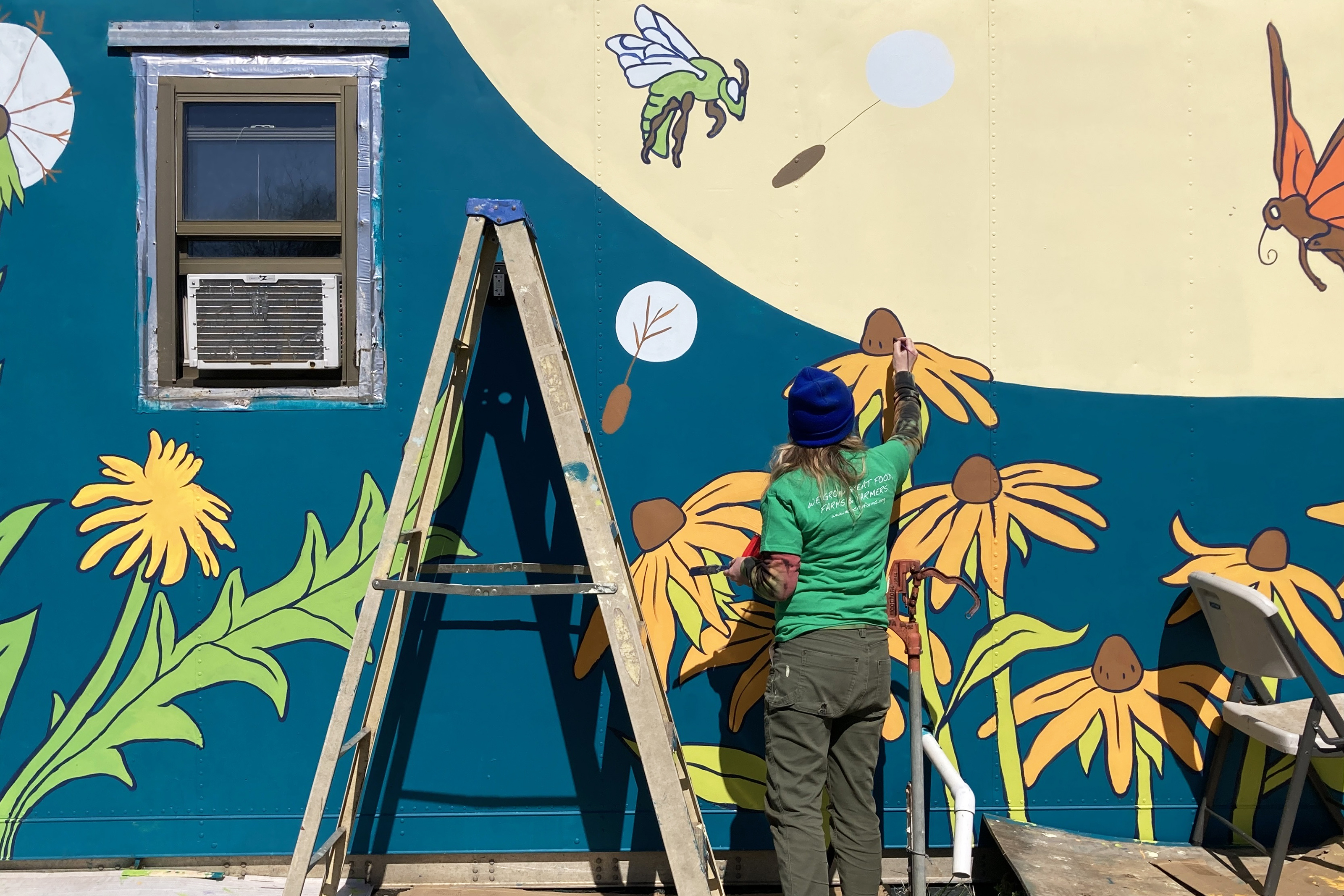 Graduate student Simone nemes stands on a ladder and paints flowers on a mural
