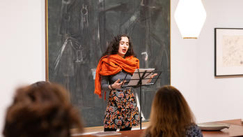 Latinx student in orange scarf giving a poetry reading.