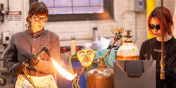 faculty member Lu Heintz adjusts a blowtorch for a student working in the Foundry
