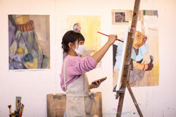 Student painting in studio with paintings on the wall.