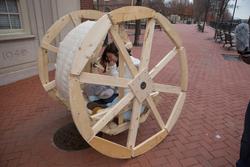 Student sitting in a large sculptural wheel