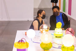 a RISD student and President Crystal Williams discuss a group of sculptural table lights on display in a gallery