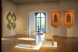 chairs sit in the middle of a gallery room, surrounded by tapestries on each side of the room