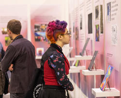 A student with pink hair checks out graphic design work at Grad Show 2023