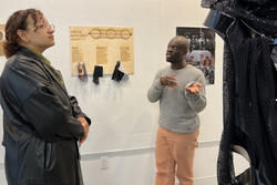 Denzel Amoah presents his Snowtown monument, three rings draped in dark fabric, while a student stands and looks at the work
