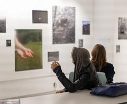 two students face several photographs mounted on a white wall