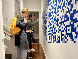 students use their phones to interact with a blue and white QR code mural printed on a white hallway wall
