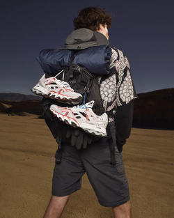 Picture of a man wearing a backpack with a pair of running shoes attached to it in a desert.