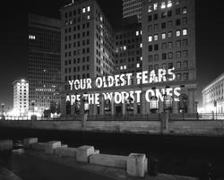 Black and white photo of a projection of the word "Your Oldest Fears Are Your Worst Ones" on the side of a building.