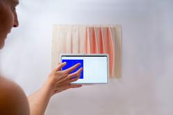 Person using tablet to control the movements of a pink and white textile.