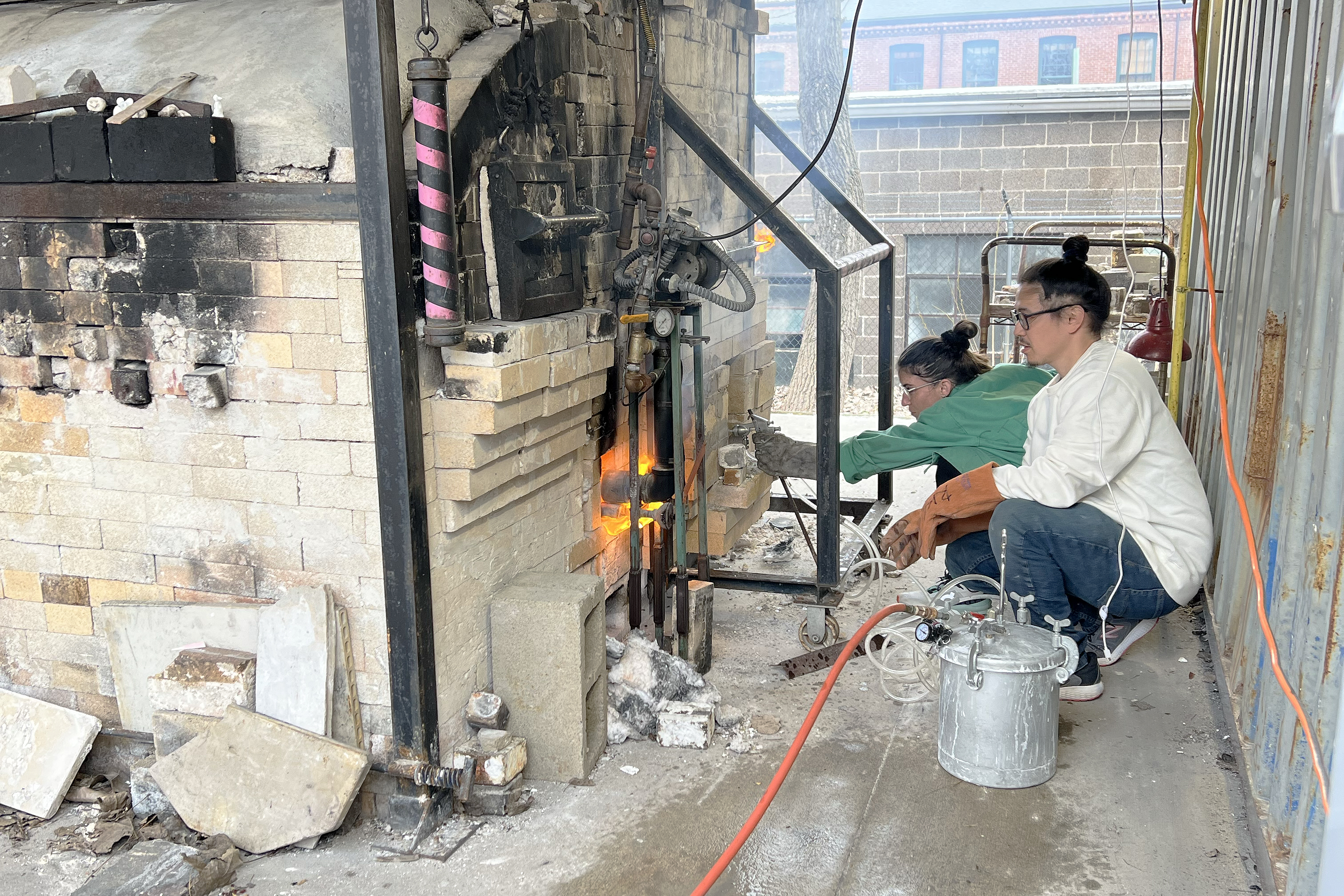 grad student Katharine Frank and tech Nicholas Oh spray bicarbonate of soda into the massive soda kiln midfire