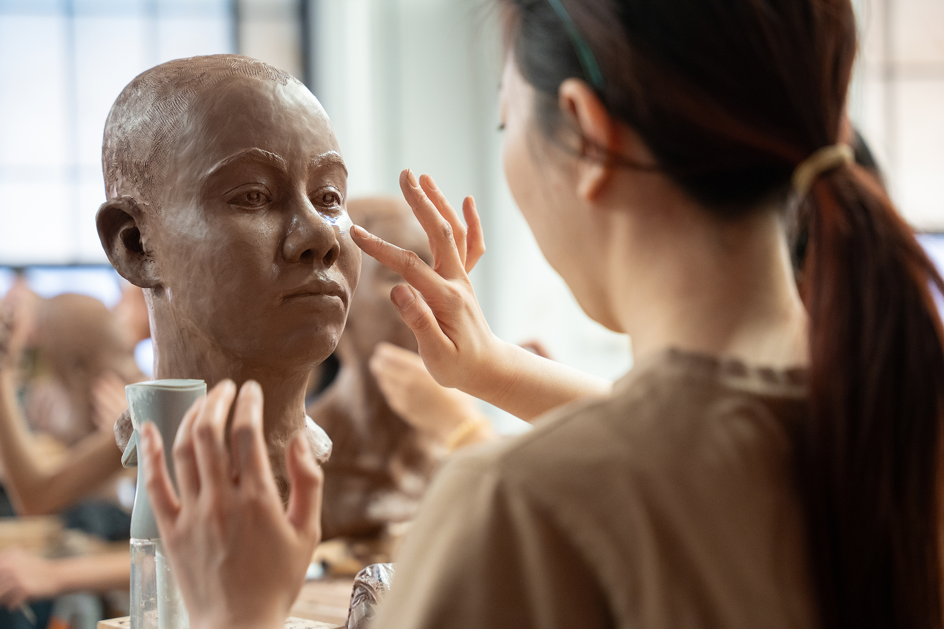 a student uses her finger to smooth out the cheek on the clay head she is sculpting