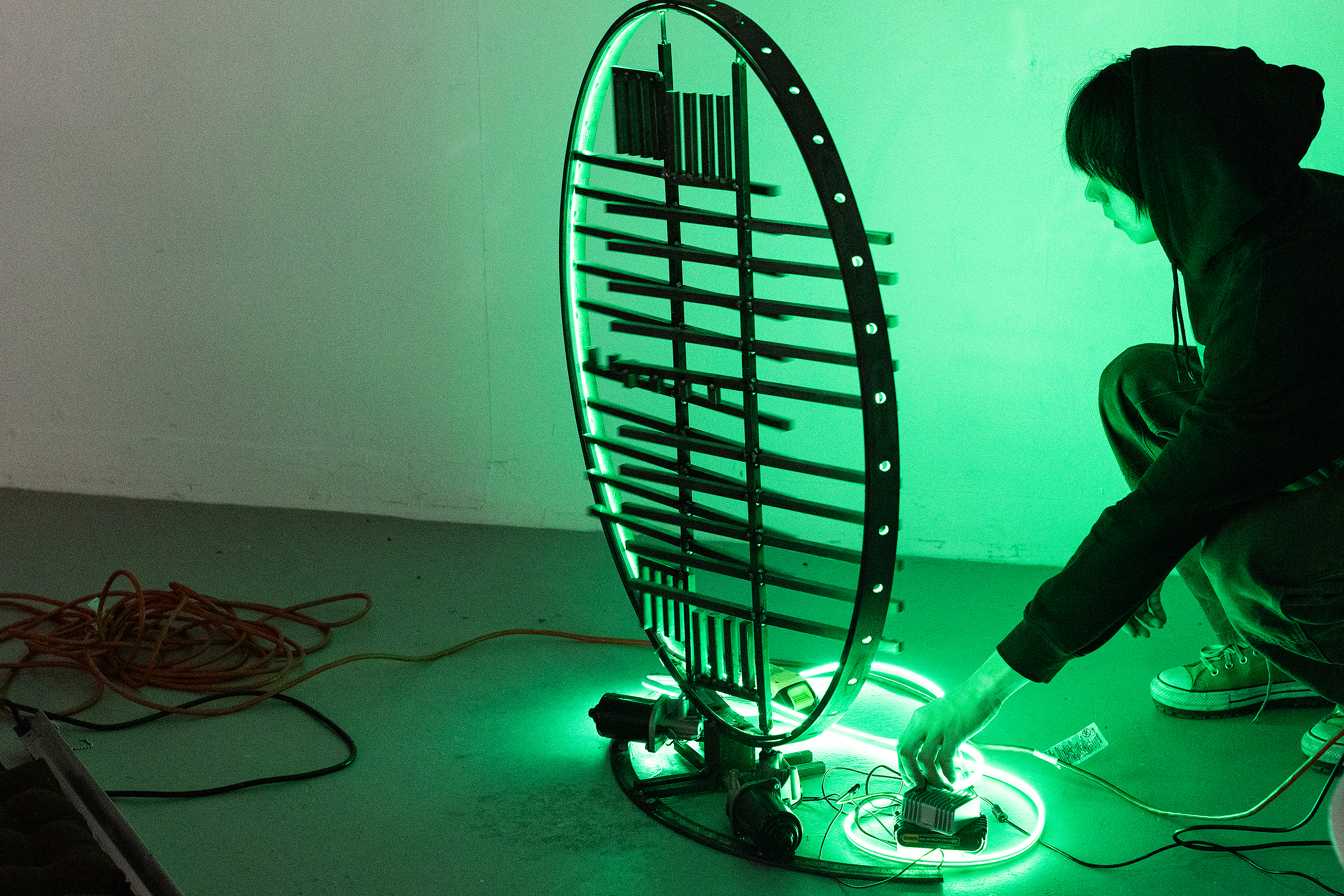 a student shows an immersive sculpture incorporating a green light in a darkened room during crits