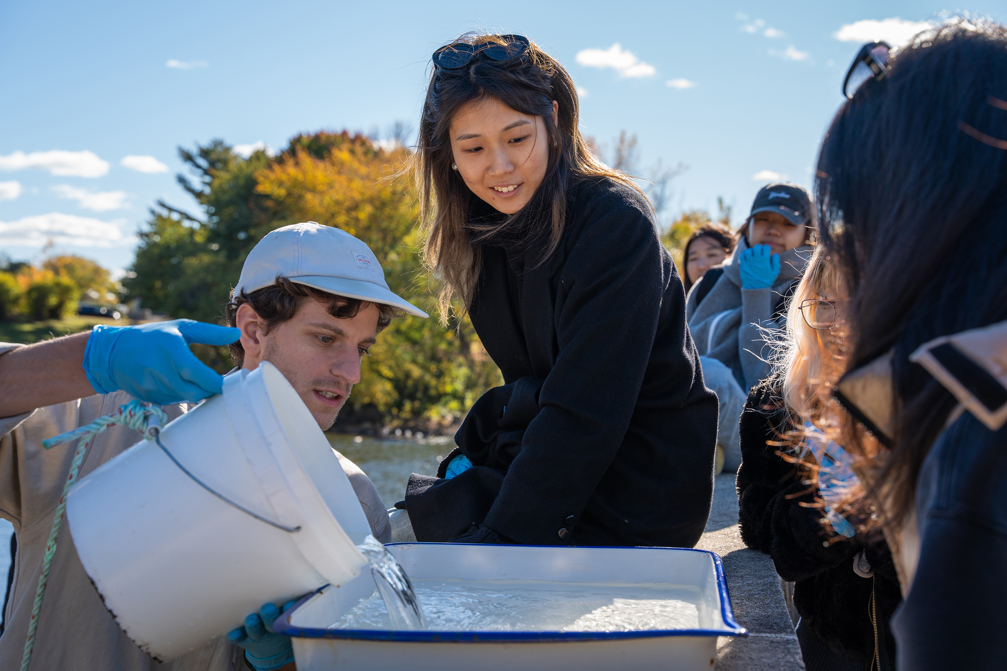 Max Pratt pours river water into a tray as students prepare to examine it