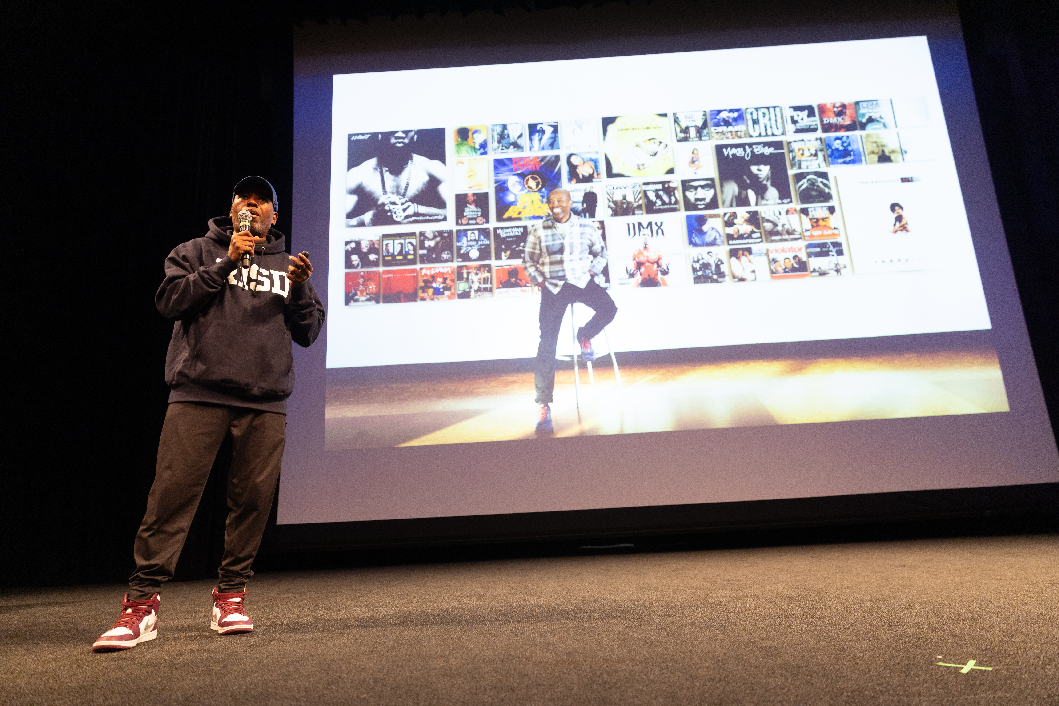 Cey Adams stands on stages in front of a presentation with all of his album art work