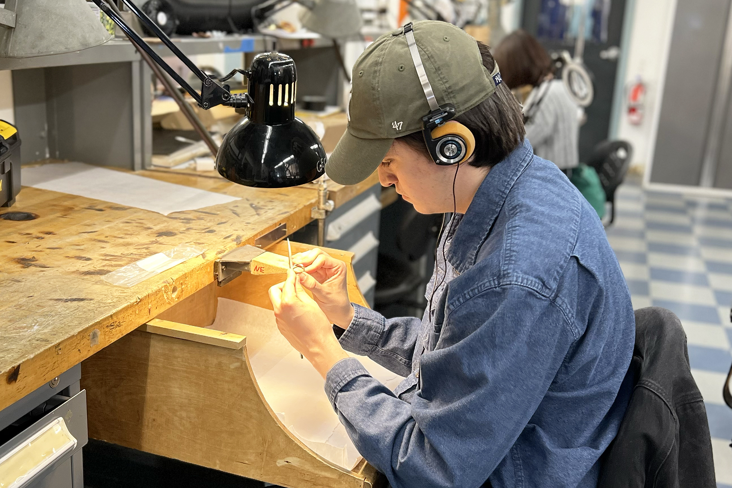 a student wearing headphones files a platinum ring at his bench