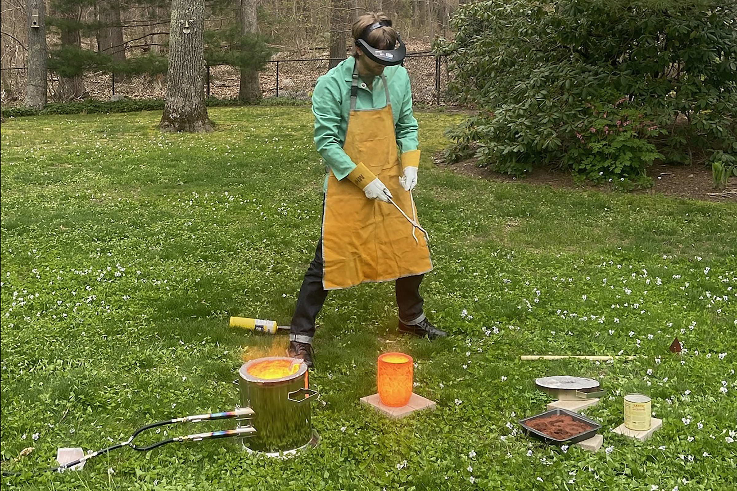 Maxwell Fertik working with molten aluminum on a green lawn
