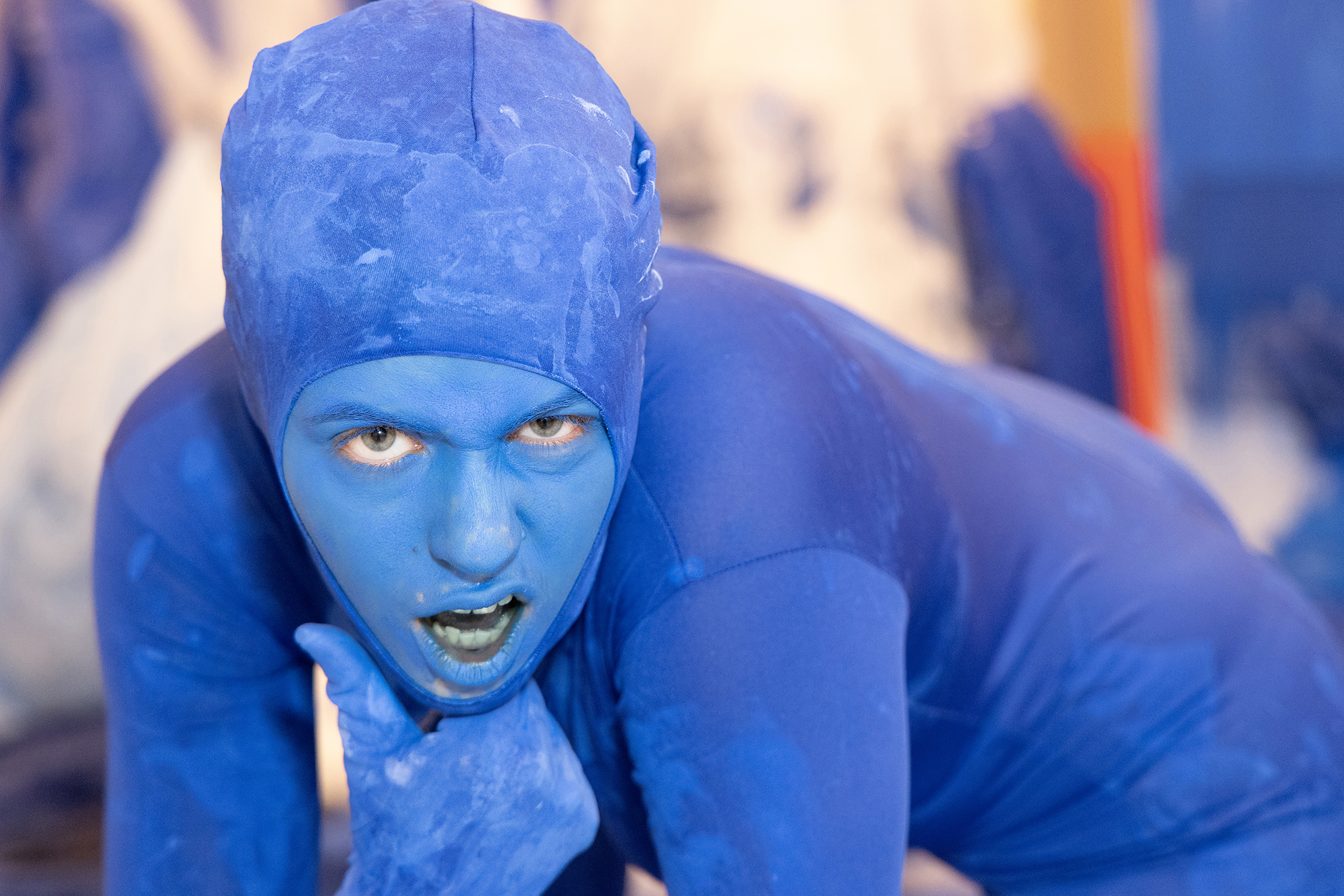 a student in blue face paint and body suit mid-performance