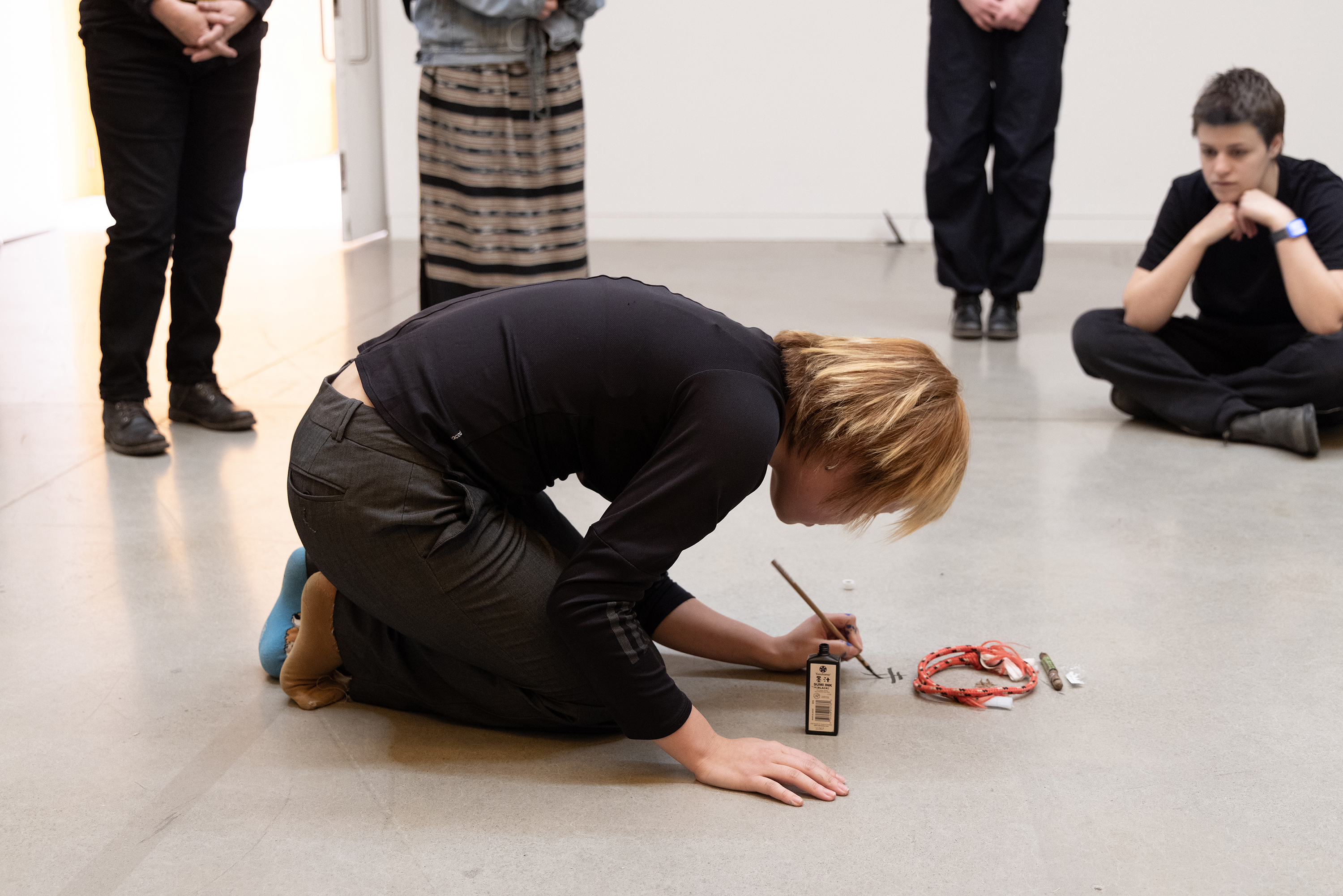 a student paints Japanese characters on the floor as part of a performance piece