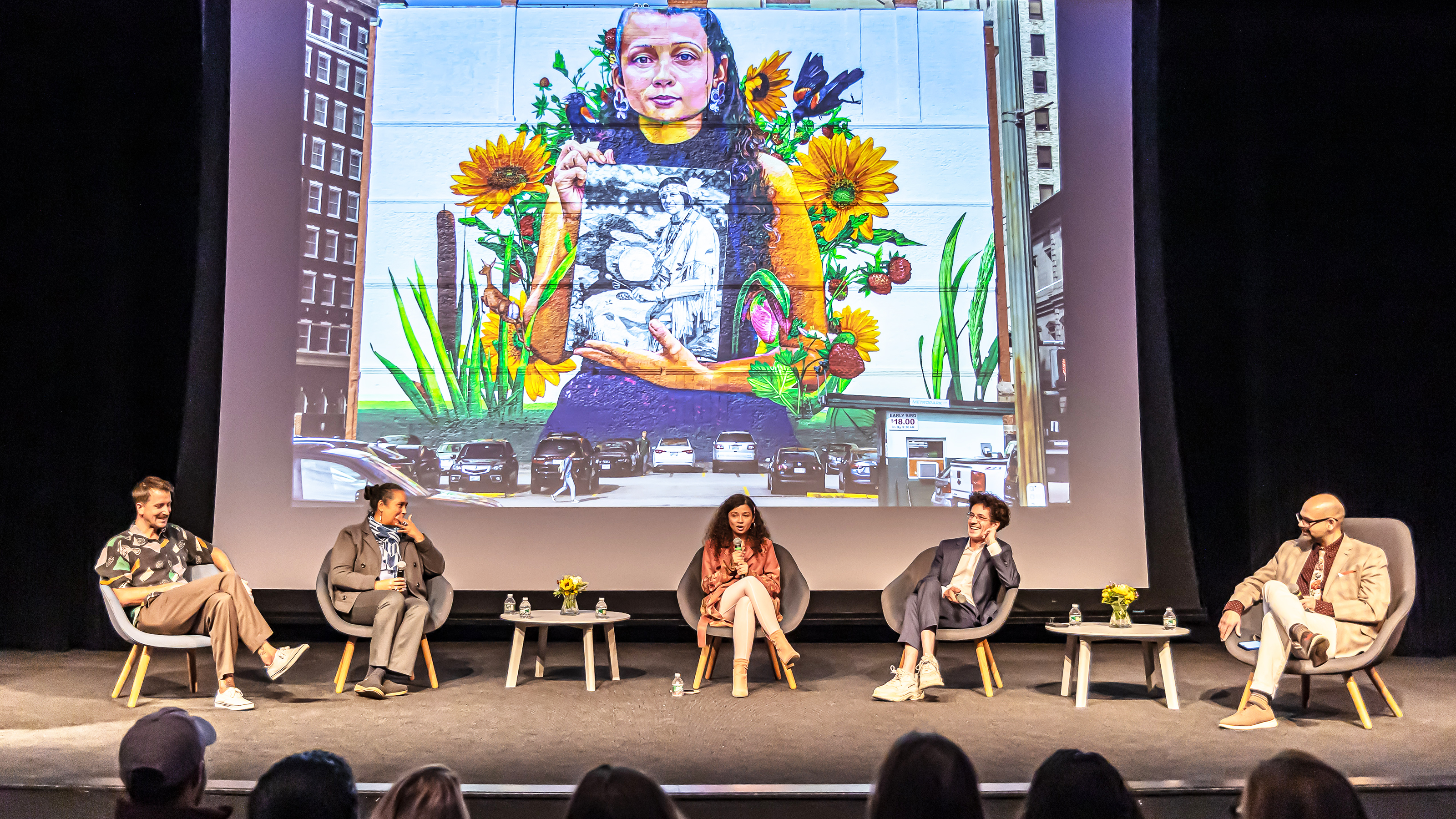 panelists on stage in the RISD Auditorium in front of projected image of Still Here mural