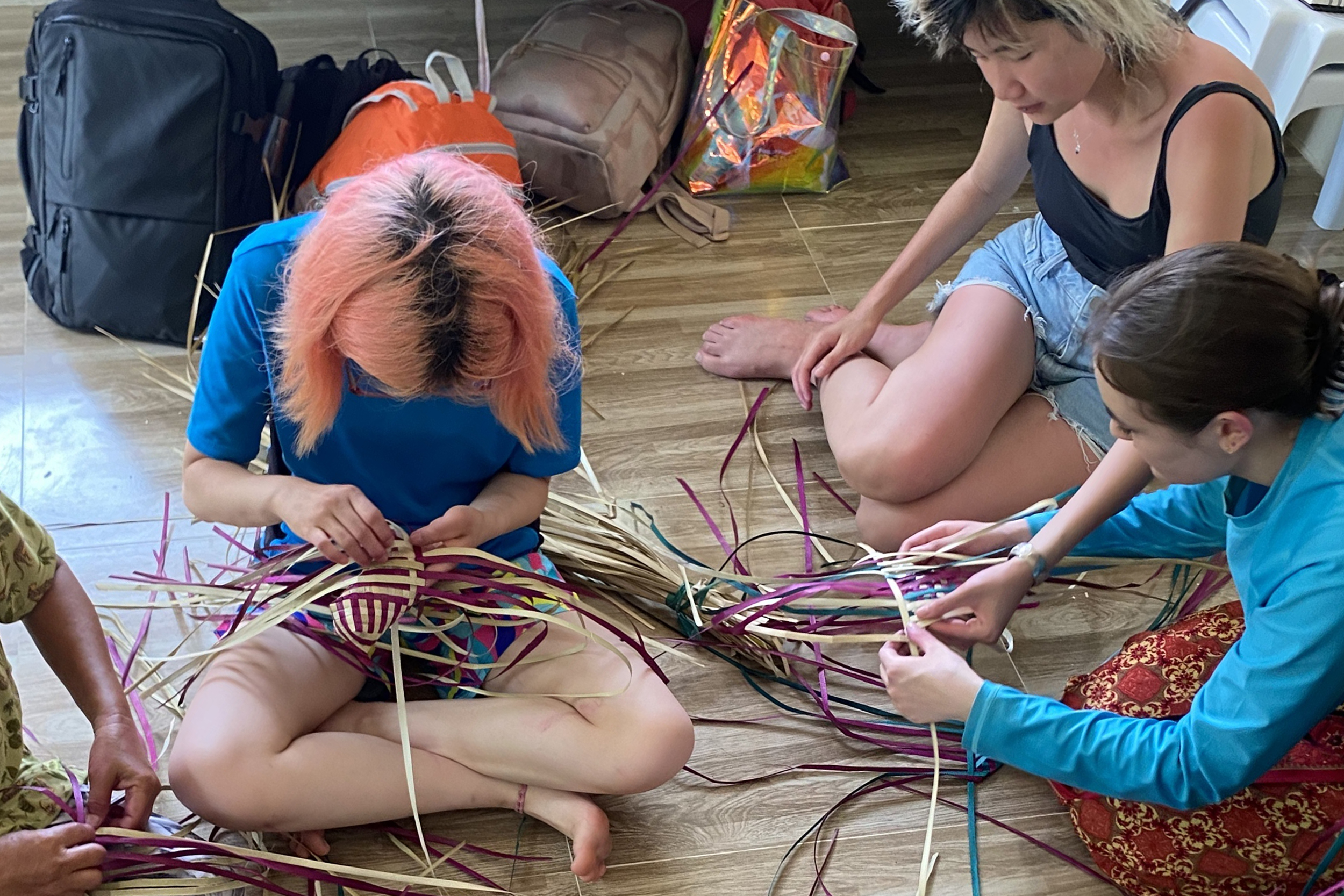 students sit cross-legged on the floor weaving traditional Filipino Banig mats