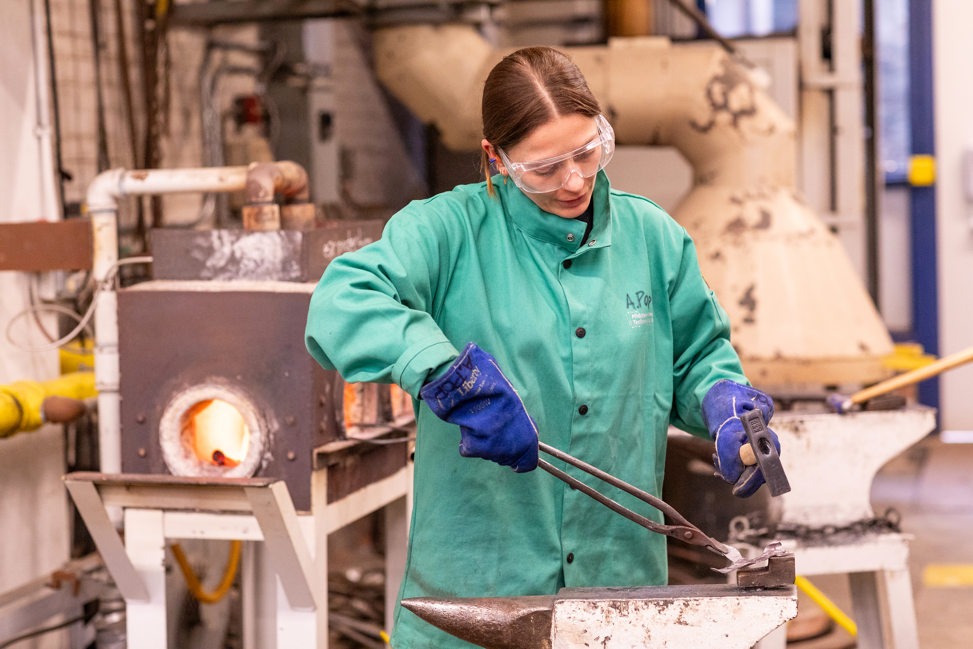 a student works in the Foundry using tongs and a hammer