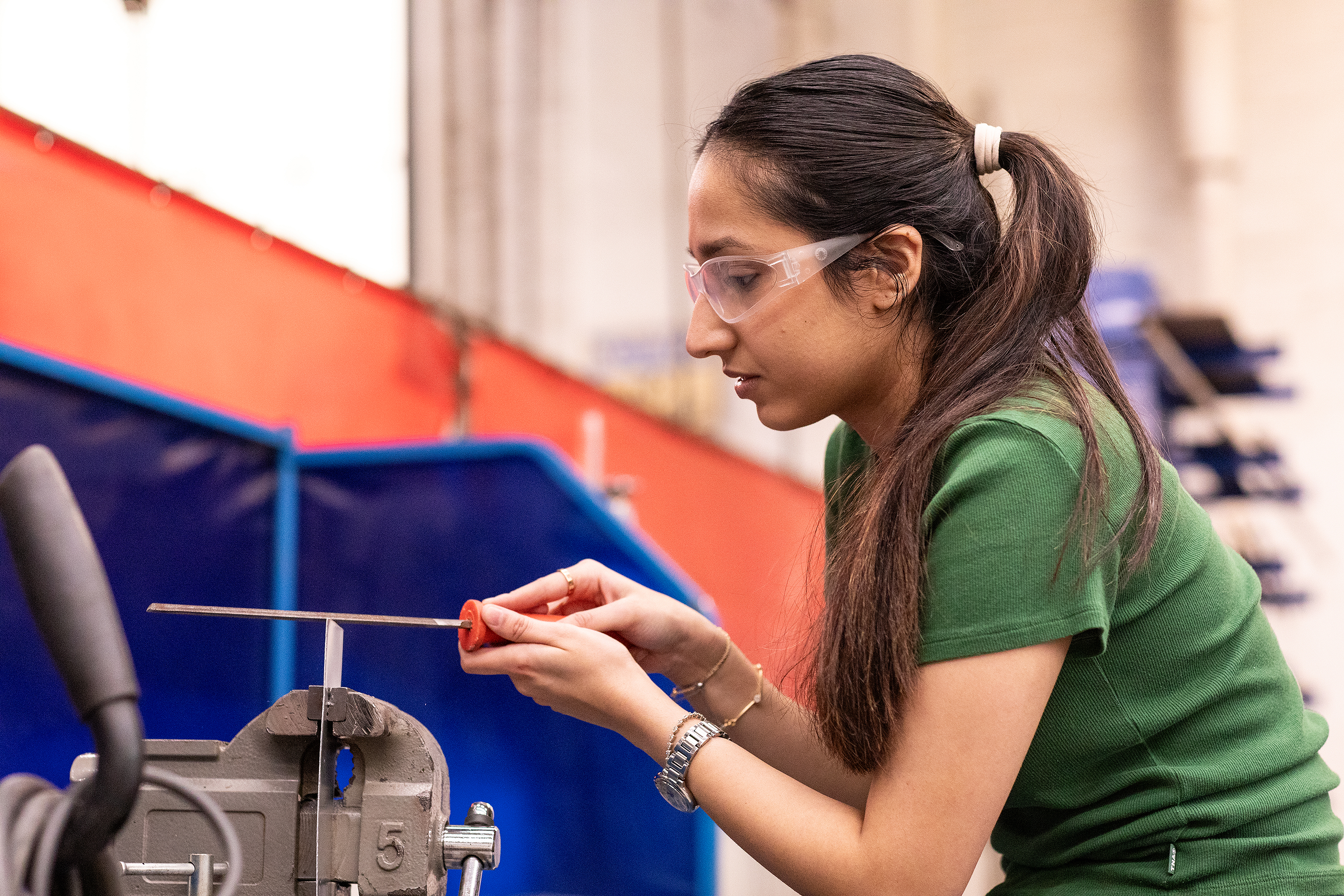 a student files down a metal piece in progress in the Foundry
