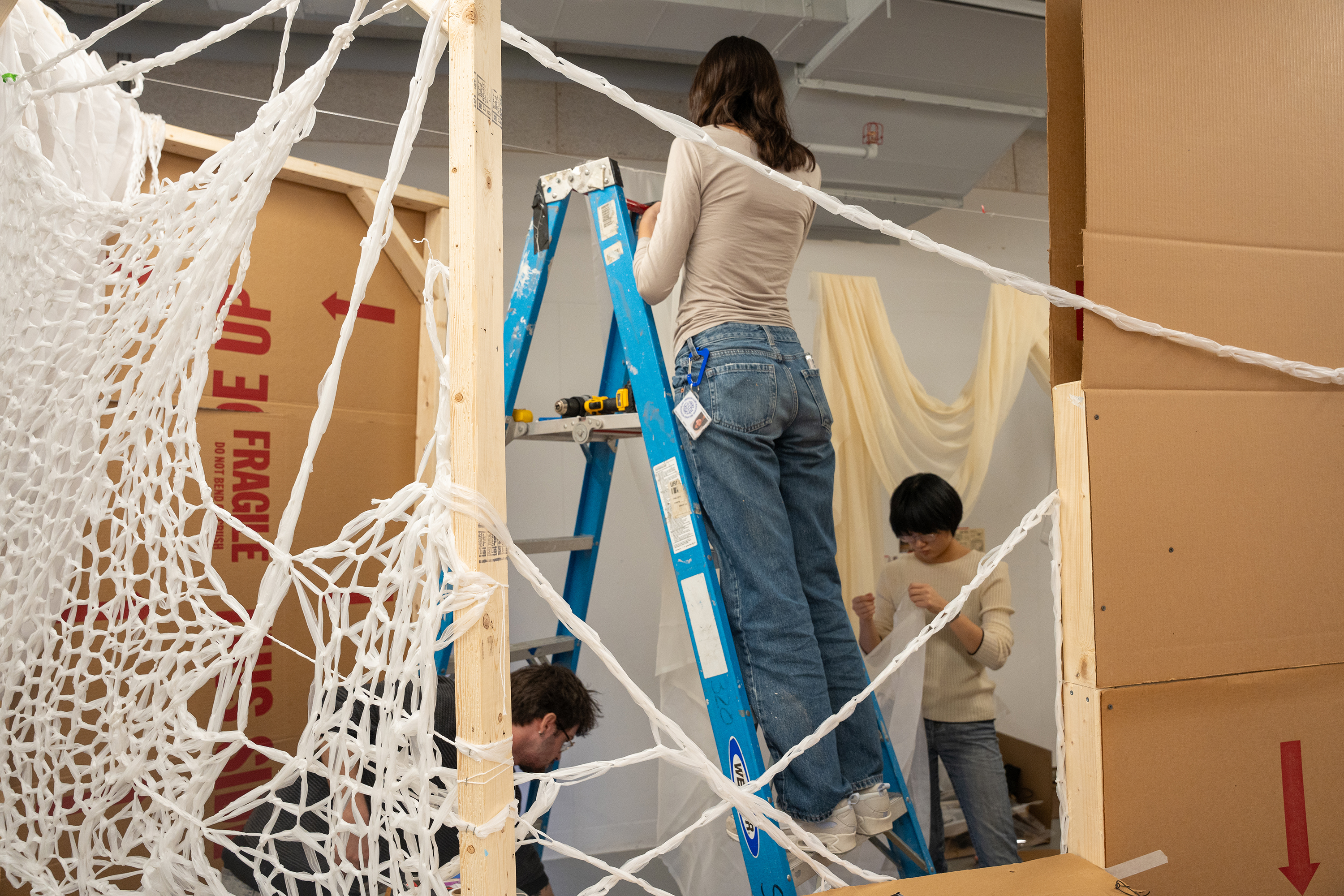 a student climbs a ladder to work on group installation piece