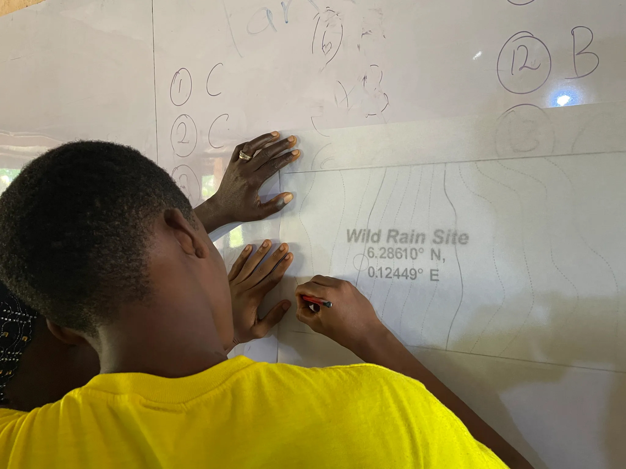 Person in yellow shirt traces map lines on a white board