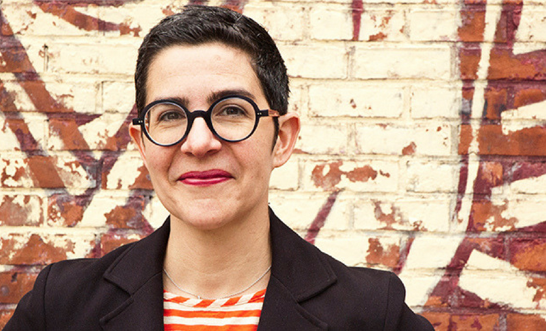A smiling Sarah Durham wearing chunky glasses.