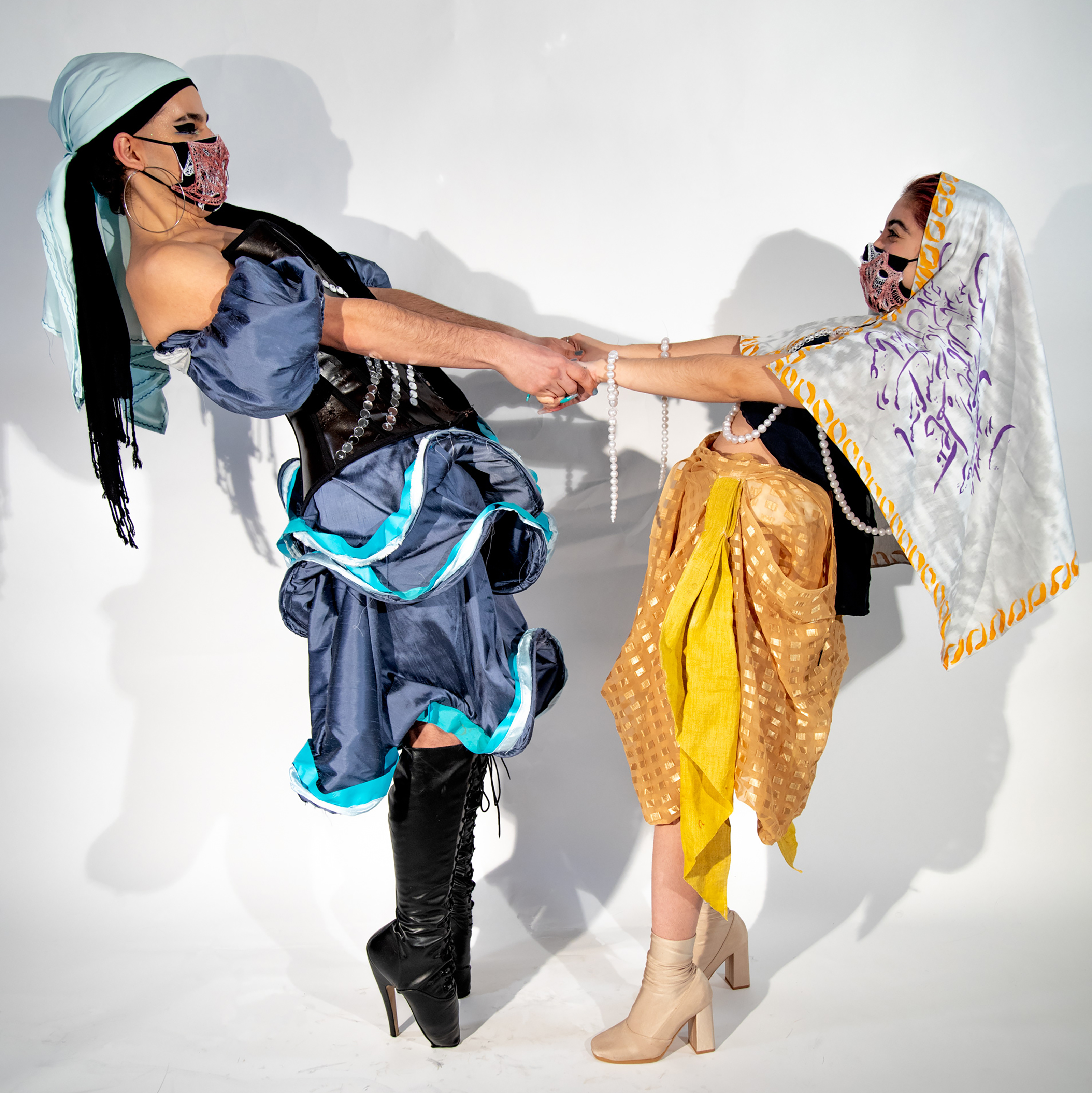 Two models holding hands and leaning back while in blue and yellow draping garments by Seabass Immonen