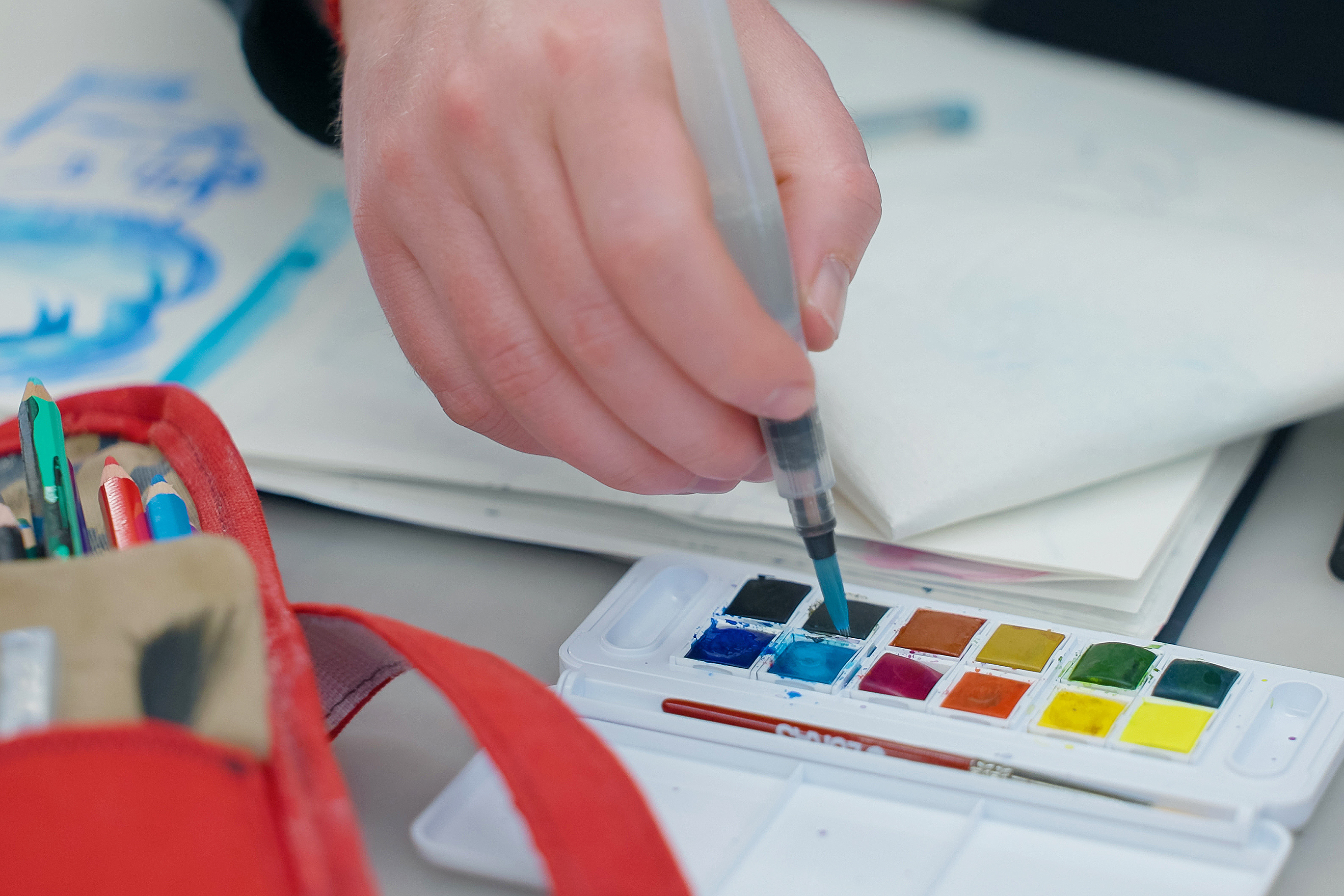 close-up of someone dipping a brush into a set of watercolor paints
