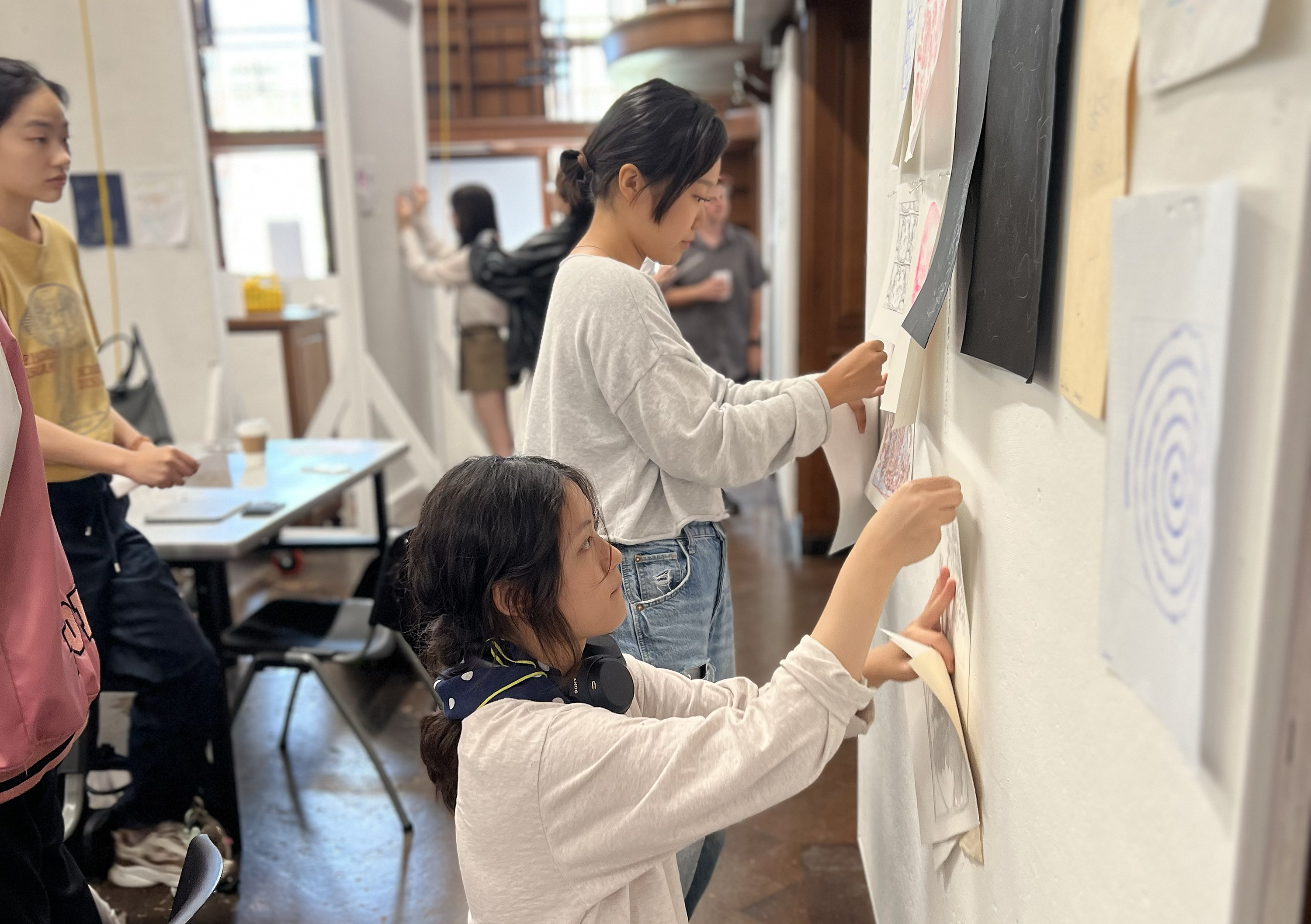 two female students pin work to the wall for critique
