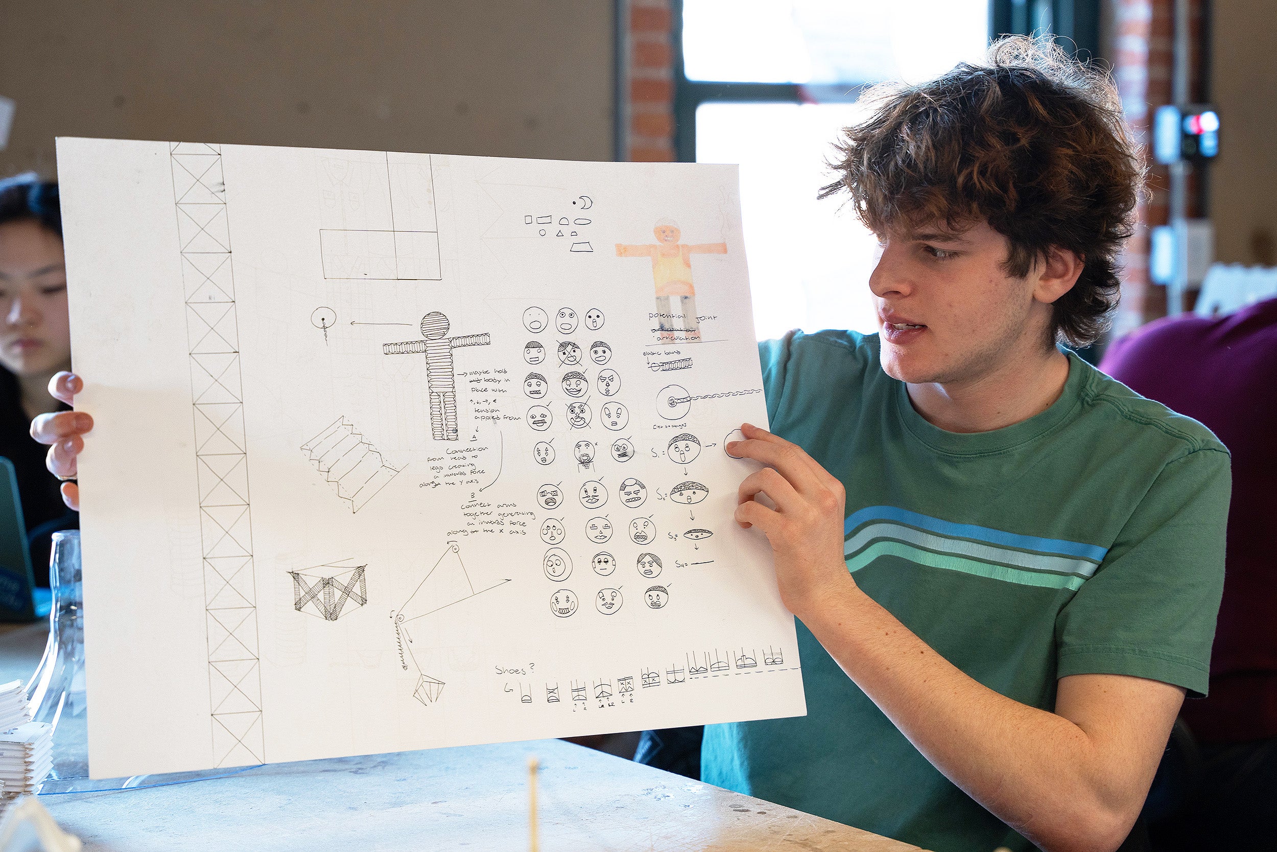 a student holds up a page of sketches that helped design his toy