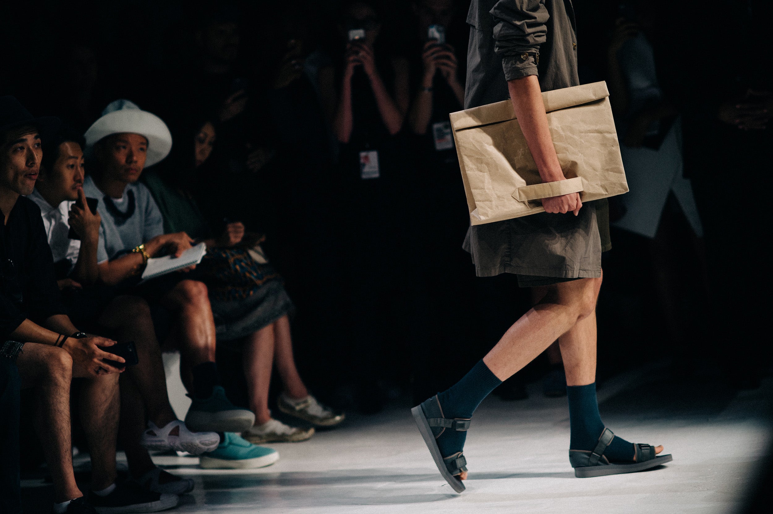 male model on the runway in socks with sandals and a paper-bag-like tote