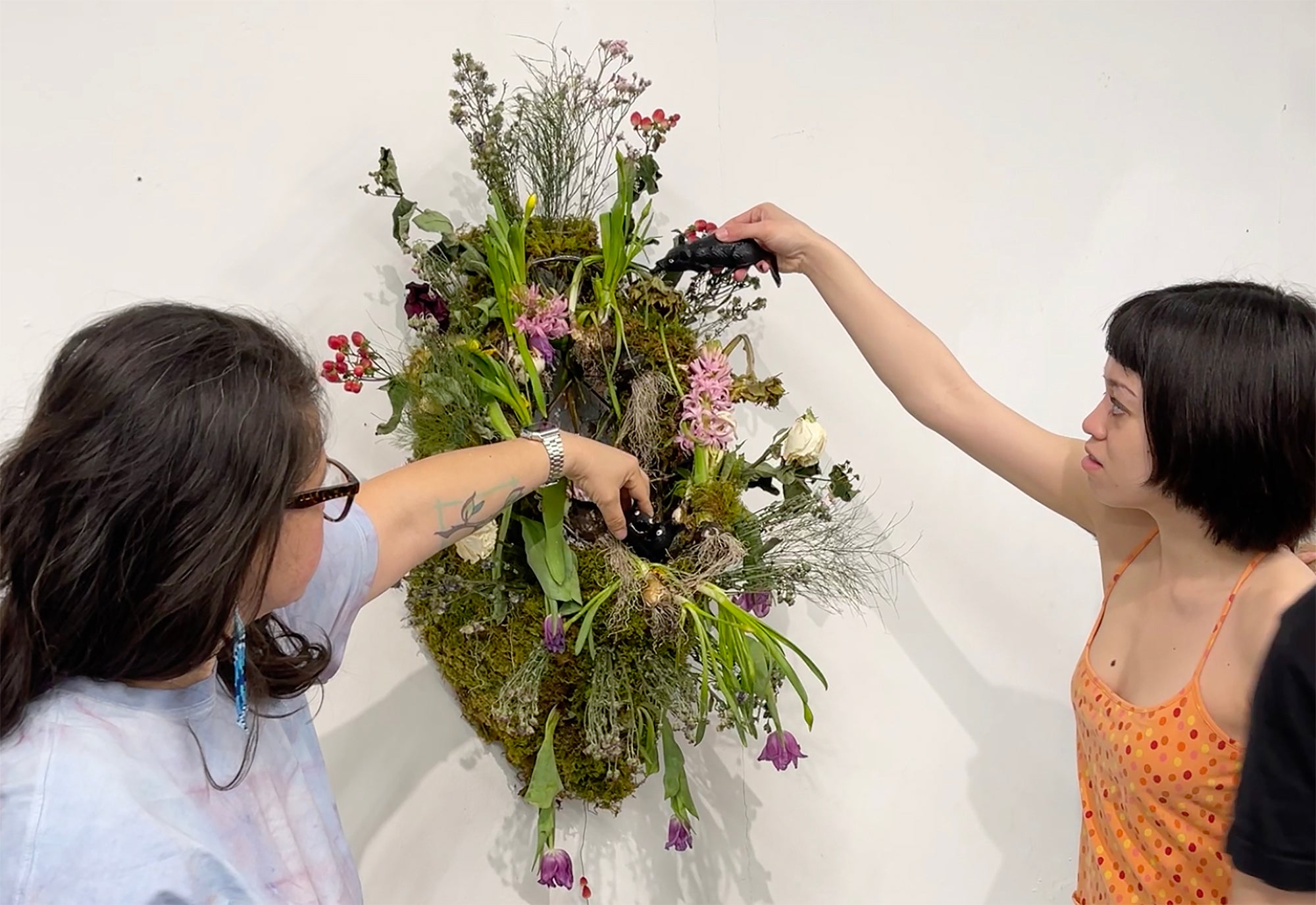members of the group interact with an installation made of flowers and a urinal