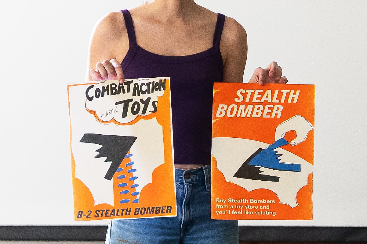 a student holds up ads for an imaginary stealth bomber toy for kids