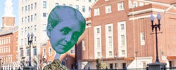 Small paper cutout of Helen Metcalf's head held up in front of RISD buildings