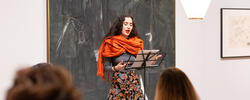 Latinx student in orange scarf giving a poetry reading.