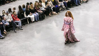 model with curly red hair walks down a runway in a pink and pillowy gown surrounded by audience members