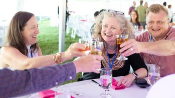A group of people are toasting together at a table during RISD's reunion weekend.