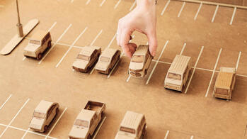 a hand manipulates tiny cardboard cars