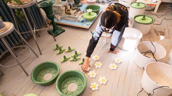 a student lays out parts to assemble a series of green-and-white, functional ceramic sculptures