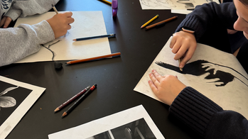 overhead closeup of student hands working on black-and-white illustrations