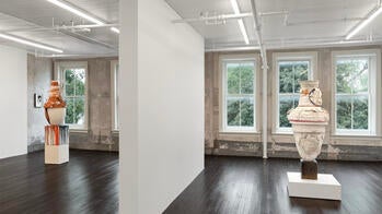 two vase-shaped sculptures stand on podiums on either side of a gallery wall, in front of several windows